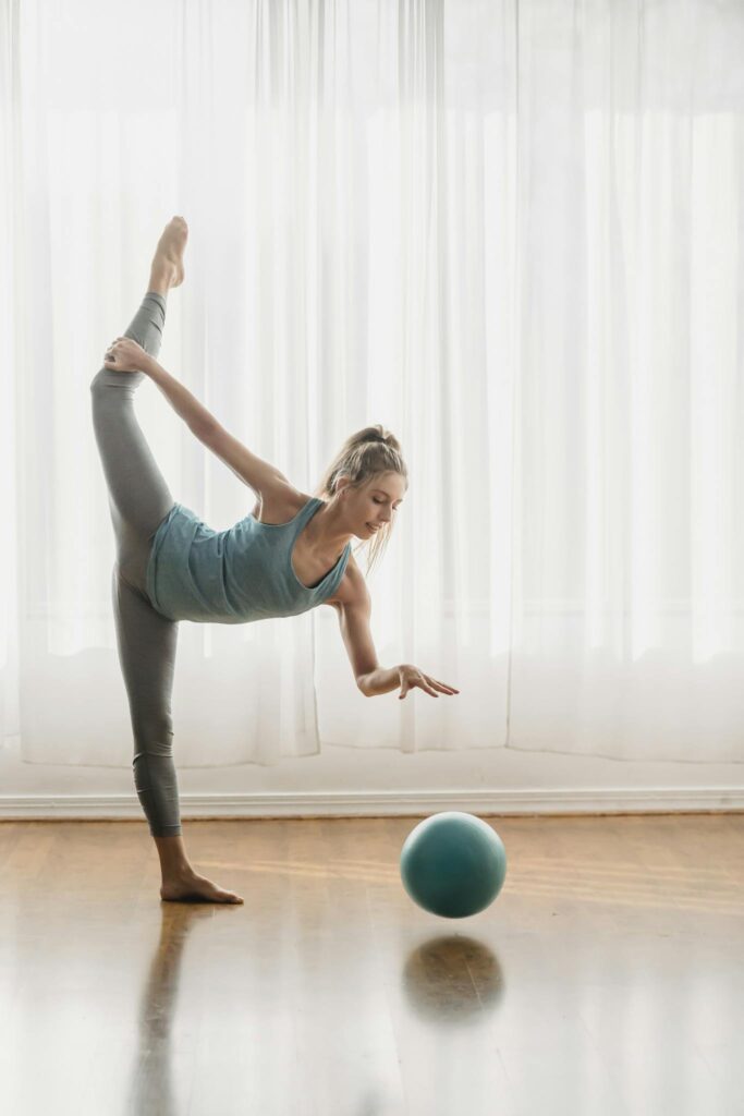 A woman demonstrating a yoga pose with a balance ball in a well-lit studio.