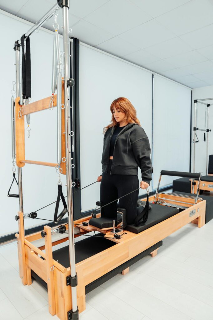 A woman practicing Pilates on a reformer machine in a studio, focusing on fitness.